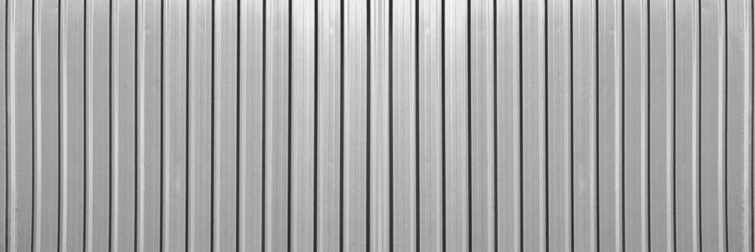 grey silver gray corrugated metal wall background texture with vertical lines and rivets. Clean industrial surface for construction or architectural backdrop. Frontal view with bright natural light.
