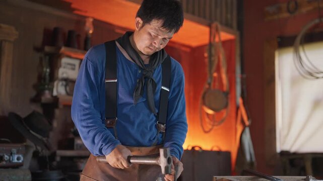 The blacksmith man with cowboy costume work in the workplace to make good metal product and he concentrate with his work.