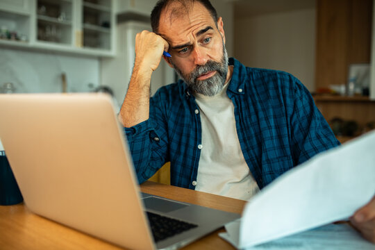 Concerned middle-aged man reviewing bills at home