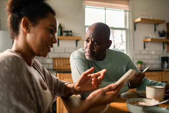 Couple discussing finances on smartphones at kitchen table