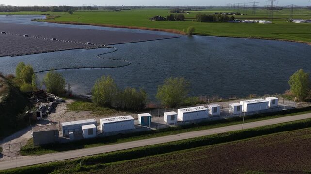 Aerial view of a floating solar panel farm on a lake next to a battery energy storage system, an innovative solution for renewable electricity production in a rural dutch countryside landscape