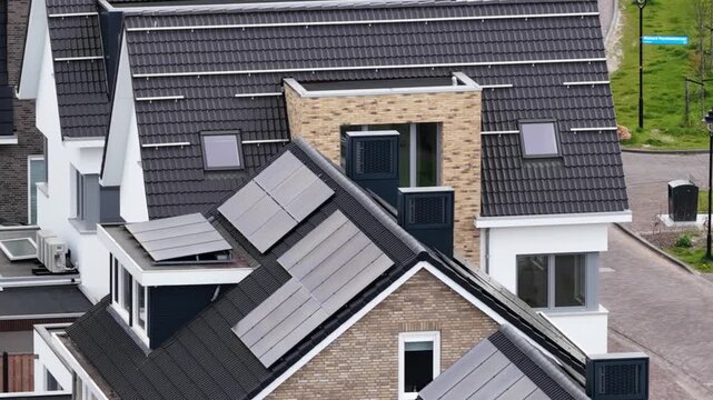 High angle view of a contemporary suburban neighborhood with modern houses featuring dark tiled roofs equipped with solar panels for renewable energy and skylights for natural lighting