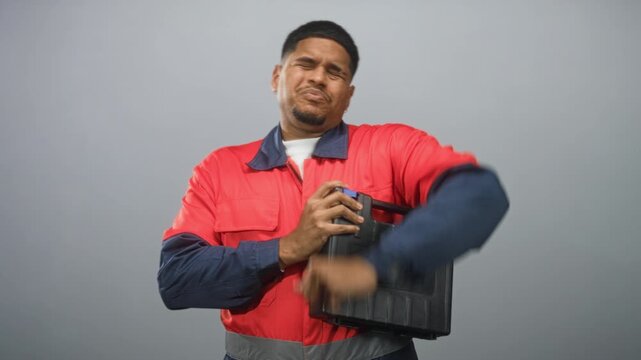 Man with beard in red work uniform clutching chest and holding toolbox in studio, wincing in pain; distress fatigue.