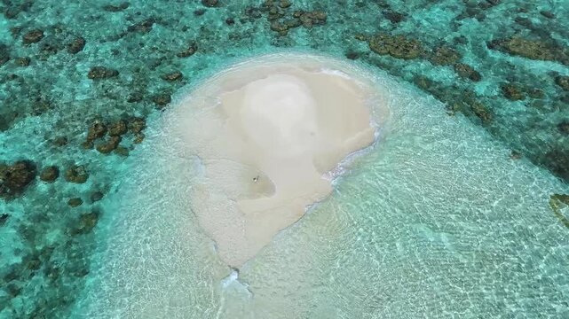 Aerial view of a tiny white sandbank with a person standing on it, surrounded by crystal clear turquoise water and coral reefs in Thoddoo, Alif Alif Atoll, Maldives.