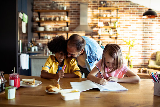 Father helping children with homework in kitchen