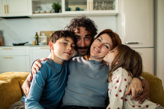 Family of four hugging on sofa in home kitchen