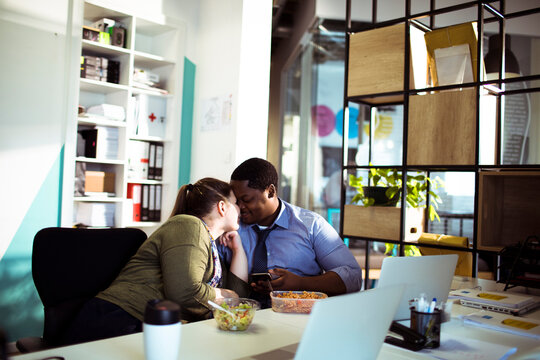 Two coworkers sharing a kiss during lunch in a modern office
