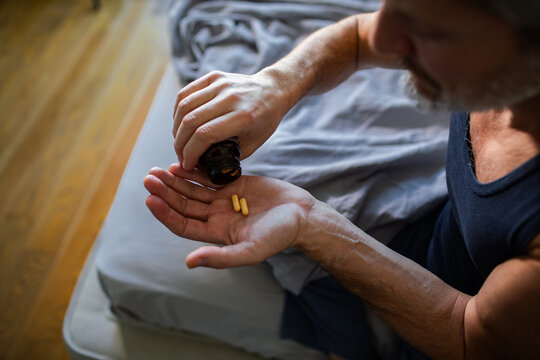 Middle-aged man taking vitamin capsules in bedroom