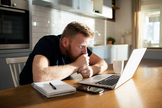 Concerned man looking at laptop in home kitchen