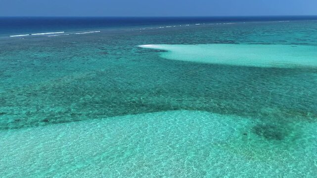 Aerial view of turquoise coral reefs, shallow sandbars, and crystal clear ocean water under a bright blue sky in Thoddoo, Alif Alif Atoll, Maldives.
