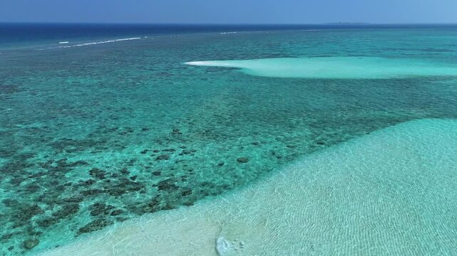 Aerial view of the crystal clear turquoise waters and vibrant coral reefs surrounding a white sandbar under a clear blue sky in Thoddoo, Alif Alif Atoll, Maldives.