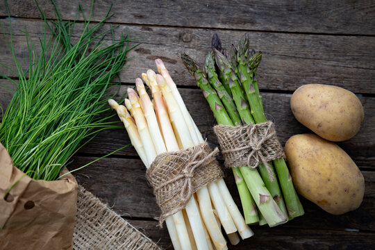 Fresh white and green asparagus with potatos on gray wood. Background for local shopping for healthy seasonal vegetables. Top view with space for text.