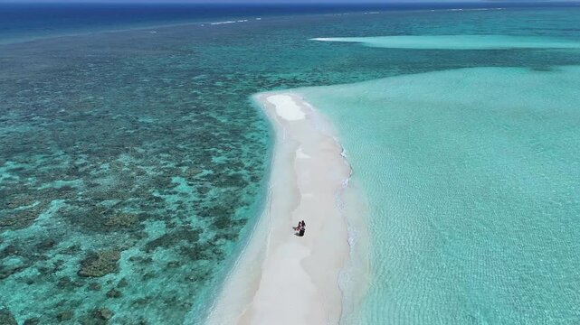 Aerial view of a person sitting on a narrow white sandbank surrounded by turquoise lagoon and coral reefs Thoddoo, Alif Alif Atoll, Maldives.