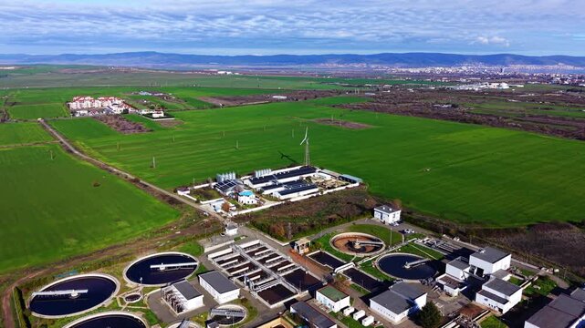 Drone shot of industrial wastewater facility with circular clarifiers and aeration tanks surrounded by agricultural landscape and residential area