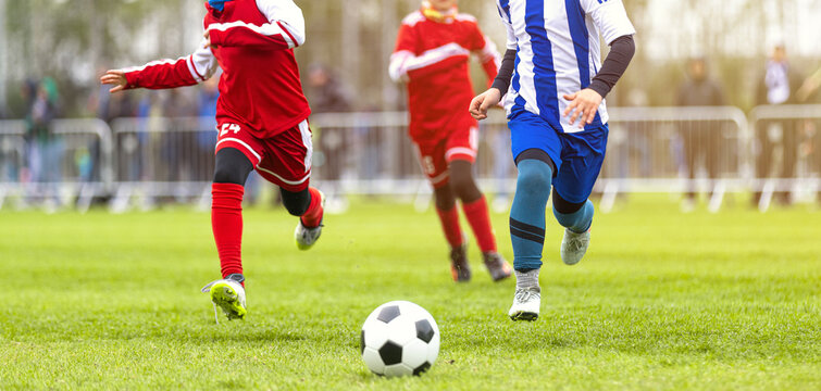 Dynamic Action Shot of Youth Soccer Players Sprinting for the Ball During Outdoor Tournament Match - Junior Athletes in Red and Blue Uniforms Competing on Pitch