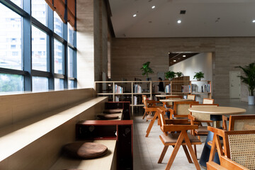 Modern library reading area featuring wooden tables, rattan chairs, and bookshelves bathed in natural light © zhu difeng