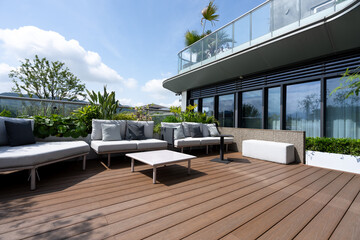 Obraz premium Modern rooftop terrace with wooden deck, outdoor sofas, green plants and glass railing under blue sky