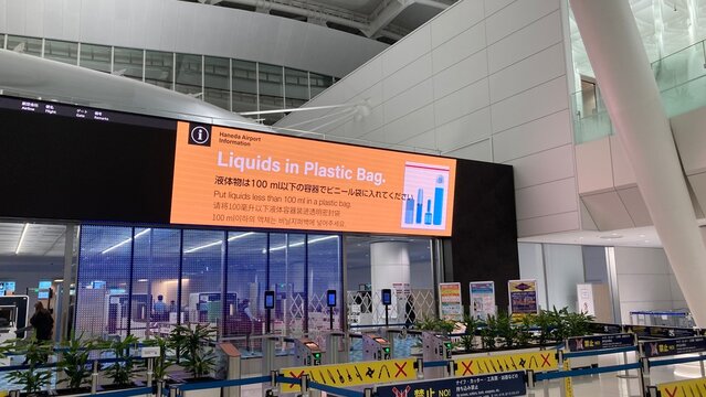 Haneda Airport International Terminal security checkpoint with large LED display showing liquid restrictions in plastic bags for passengers - Tokyo, Japan, January 30, 2024