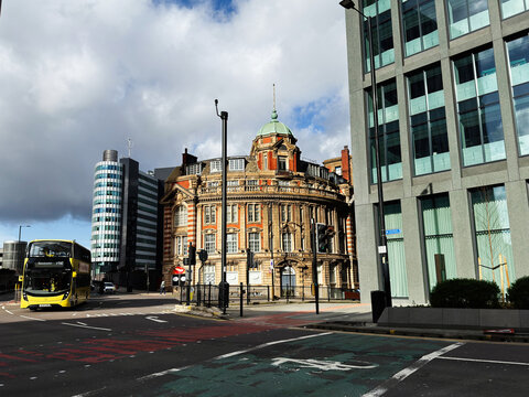 Historic red brick Parkers Hotel building and modern offices in Manchester UK with double decker bus, family with stroller and pedestrians on a cloudy city street