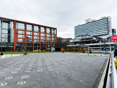 People relaxing in Manchester city square with modern office buildings, Mercure Hotel and urban plaza on a cloudy day