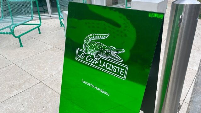 Le Cafe Lacoste branded A-frame sidewalk sign featuring the iconic crocodile logo outside the Lacoste Harajuku flagship store in Shibuya district - Tokyo, Japan, January 17, 2024