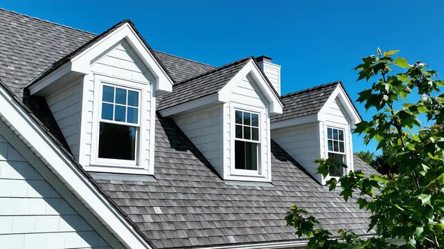 Close-up of a house roof with dormer windows and a clear blue sky.
