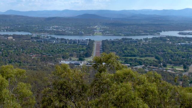 Panoramic tilt shot of Canberra city skyline with parliament house and lake burley griffin under blue sky.