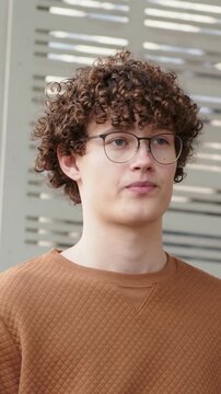 Vertical video: Straightening from lowered gaze, man scanning at walkway by panel with rust sweater