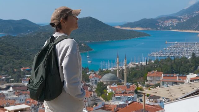 Woman with backpack admiring kas cityscape and harbor in turkey. Young female traveler with a backpack enjoying the beautiful panoramic view of the sea and the coastal town of kas in antalya, turkey