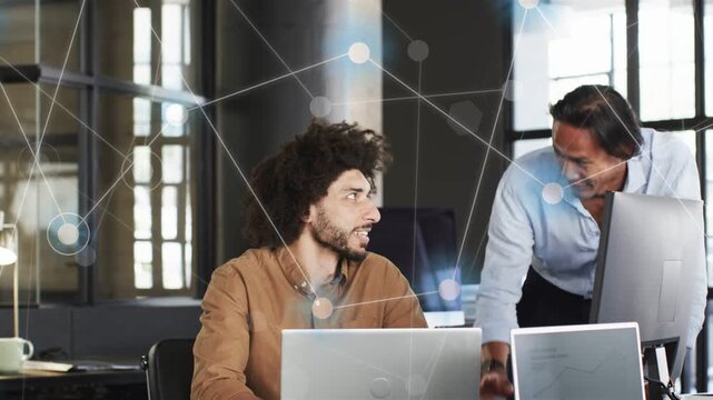 Seated man using laptop standing man leaning and pointing woman joining tablet reviewing tech plan