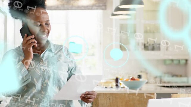 Mature woman taking call, holding paper, reviewing for tech, animated icons appearing over laptop