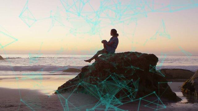 Woman stepping down beach rock into sitting, watching ocean while teal overlay signaling technology