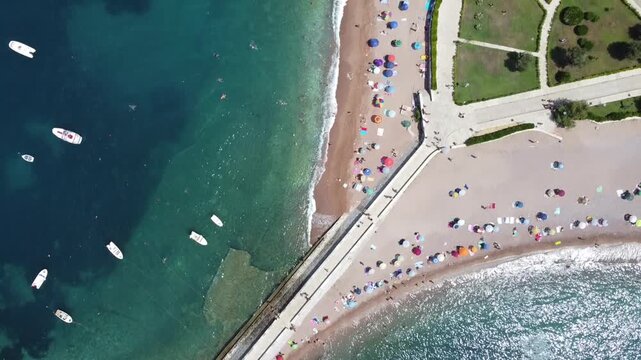 Horizontal drone footage of Sveti Stefan island in Montenegro, showing the connecting road, sandy beach, turquoise sea, and surrounding mountains
