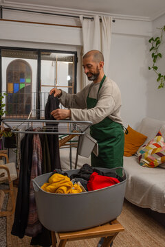 Smiling hispanic man hanging pants on drying rack at home