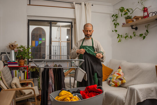 Bearded hispanic man preparing sweater on hanger for drying at home