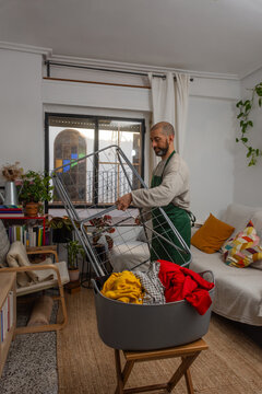 Hispanic man opening drying rack in cozy living room for laundry