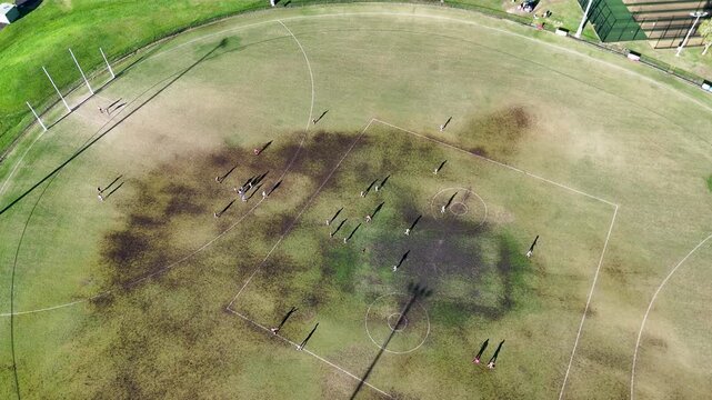 Aerial view of australian rules football players on a muddy green field in motion during daytime training or game.