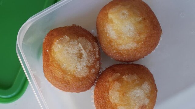 Close-up of three sugar-topped muffins in a plastic container