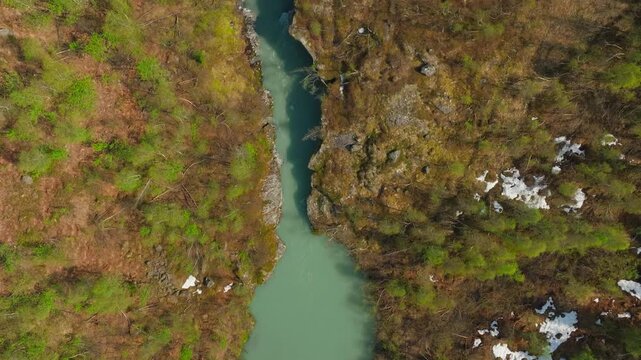 Top-down drone view of a turquoise glacier river winding through alpine tundra in Norway, with snow patches along the banks. Pristine wilderness, natural patterns, and cinematic travel scenery.