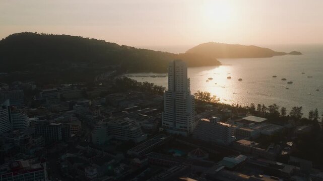 Drone approaching Patong Tower at sunset with boats in Phuket Thailand
