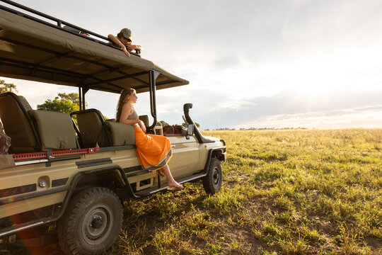 siblings on safari vehicle looking at sunset, Okavango Delta, Botswana, Africa