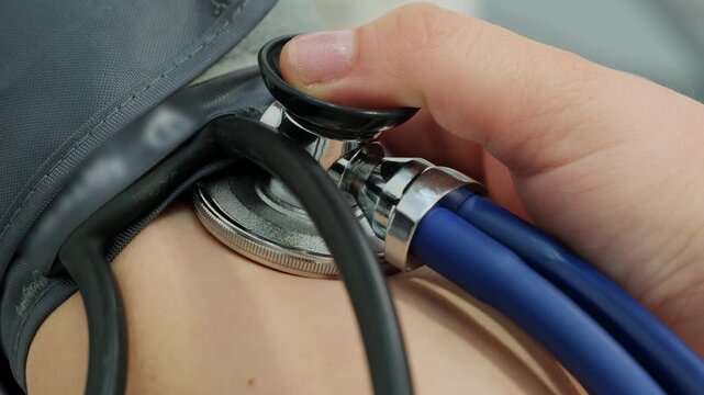 Doctor hand attaches stethoscope under blood pressure monitor cuff on patient arm closeup. Medic uses tools to check cardiovascular health