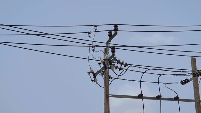 Electric power lines and insulators on concrete pole against a clear blue sky background. Concept of electrical grid, energy distribution, utility infrastructure, and industrial connectivity.