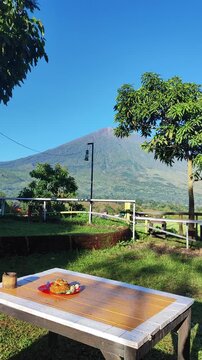 Beautiful mountain view with breakfast on the table, scenic landscape of Mount Rinjani from a hillside cafe at sunrise, peaceful morning atmosphere in rural Indonesia.