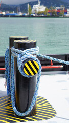 Fototapeta premium Blue mooring rope tied around a black and yellow striped bollard on a ship deck