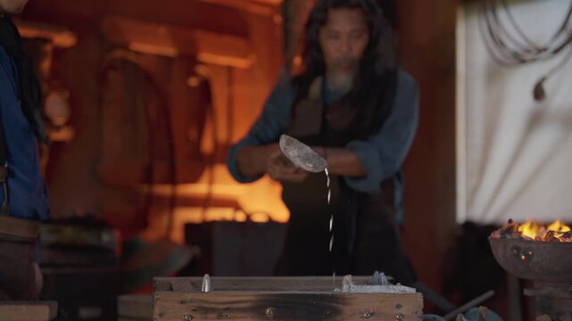 The senior man with cowboy costume work as blacksmith pour melted metal such as silver to crucible in workplace.