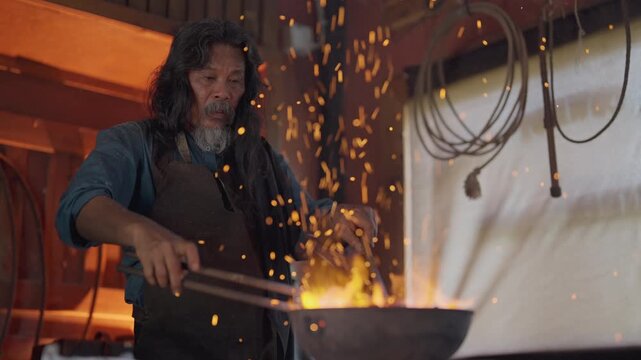 Senior man hold tools that hold horseshoe during process of strike the iron in room with fire in stove.