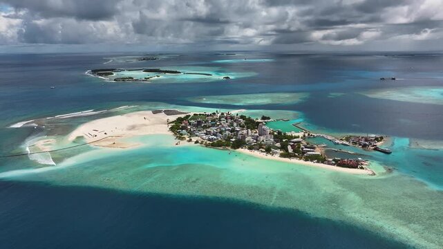 Aerial view of Gulhi island featuring turquoise lagoons, land reclamation, and local settlement under a cloudy sky in Gulhi, Kaafu Atoll, Maldives.
