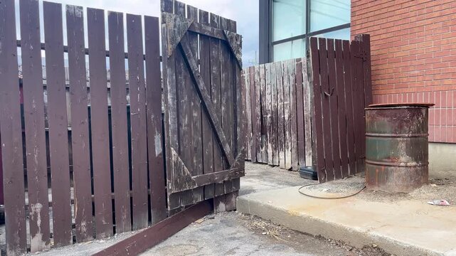 Weathered wooden fence enclosing backyard garbage area in alleyway. 