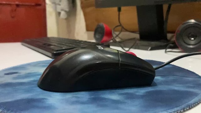 Black computer mouse on a desk mat with keyboard in background